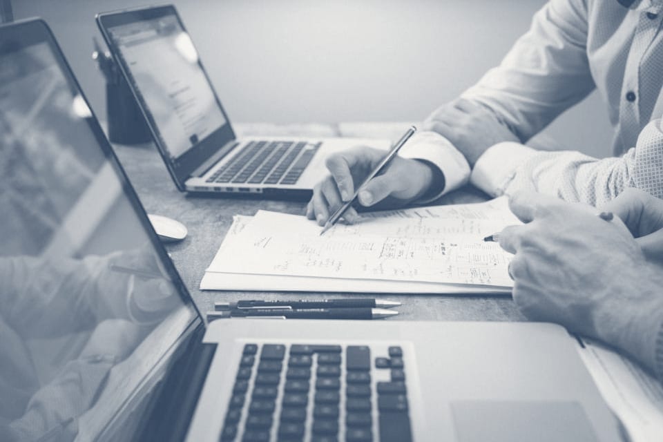 Two colleagues working through a printed plan together, laptops open beside them.